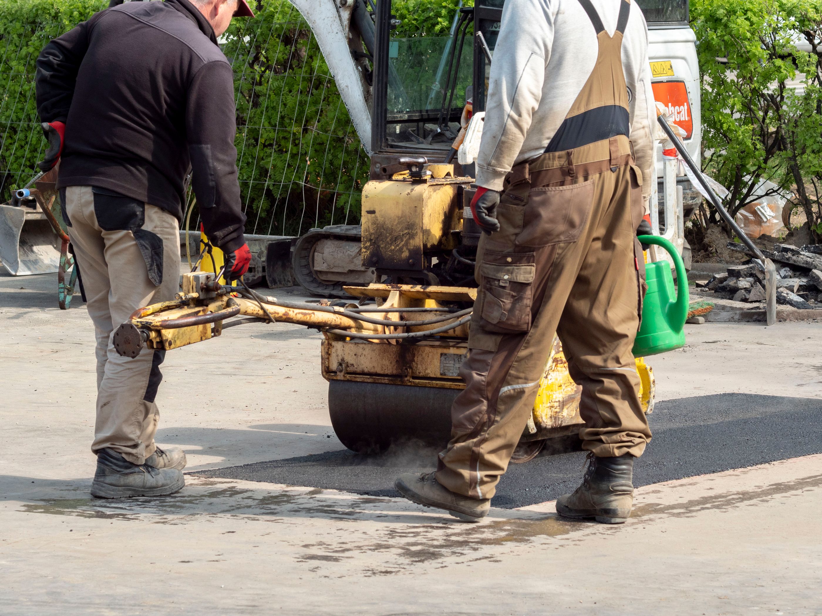Doi muncitori care repară un tronson de drum și lucrează cu același utilaj